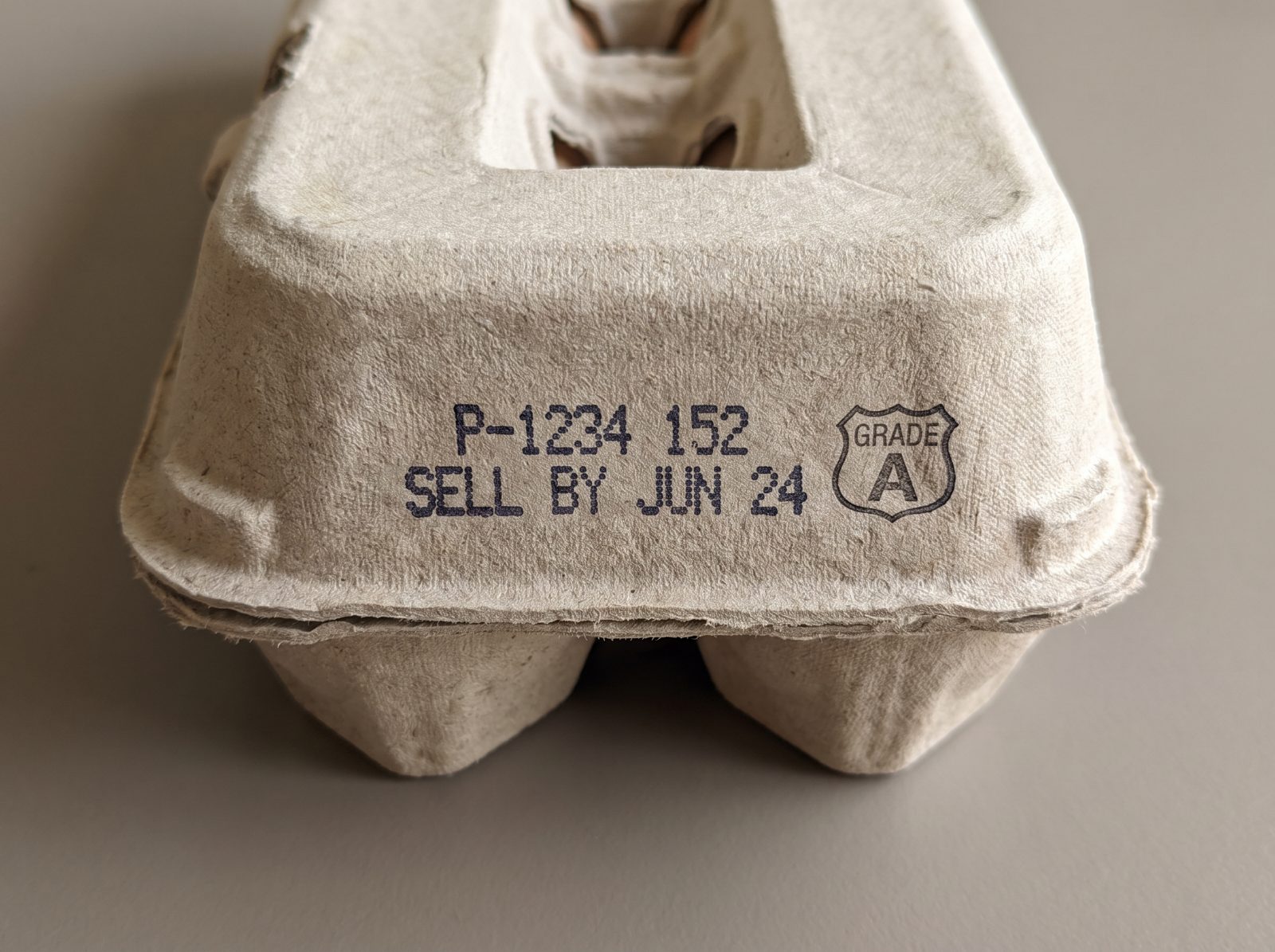 Macro photograph of the back of an egg carton showing the stamped code and grade shield